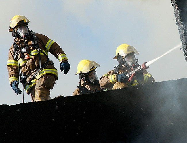 燃烧塔上三位消防员运行水管满足ISO培训需求